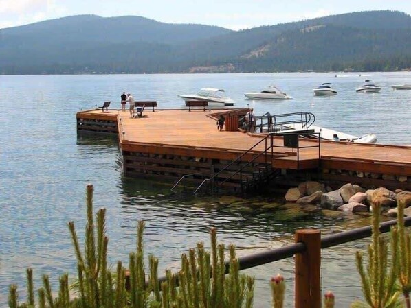 A dock with boats, a wooden pier, and a calm lake with mountains in the background.