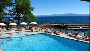 A swimming pool with people, umbrellas, and a view of the sea and mountains. - Brockway Springs Lake View Unit- #30 (Kings Beach)