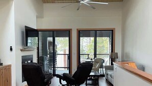 A spacious living area with a ceiling fan, a dining table, two black chairs, a sofa, and a kitchen area with a countertop. - Brockway Springs Lake View Unit- #30 (Kings Beach)