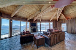 A spacious living room with a fireplace, leather sofas, and large windows overlooking a body of water. - Brockway Springs Lake View Unit- #30 (Kings Beach)