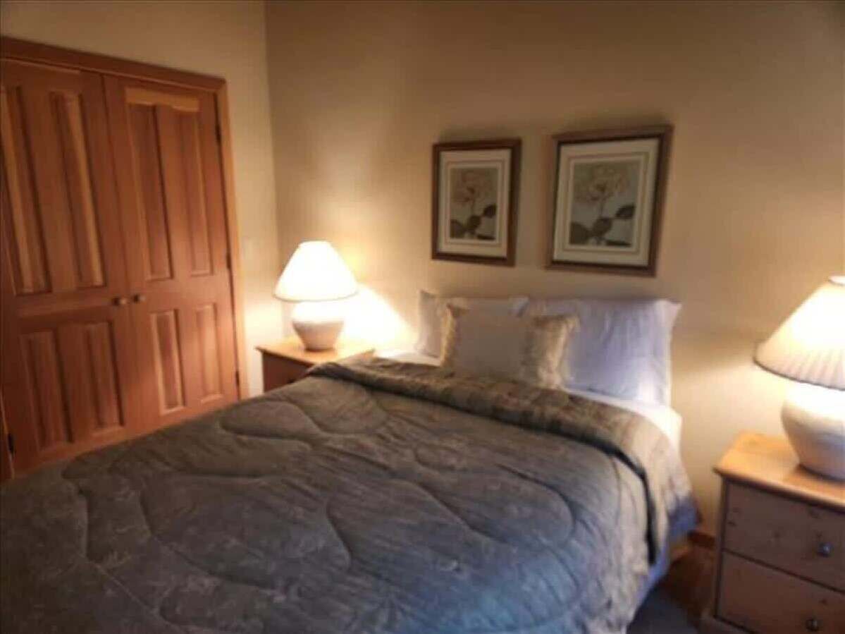 Une chambre à coucher avec un lit, deux lampes de chevet, une armoire en bois et deux tableaux encadrés accrochés au mur.