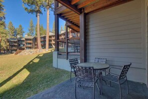 A covered outdoor seating area with a table and chairs, overlooking a building with multiple balconies and a grassy lawn. - Lakefront Condo in Kings Beach- #43 (Kings Beach)