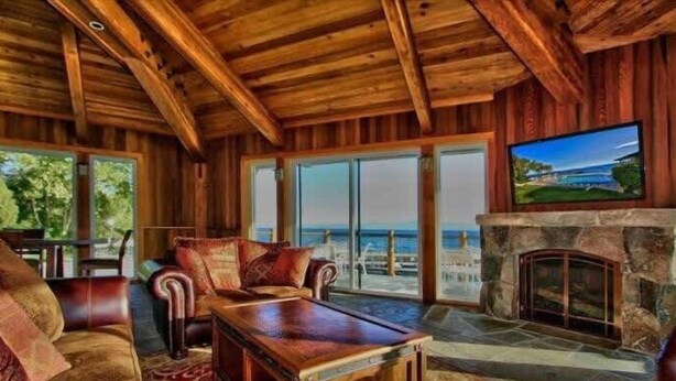 A wooden interior with a stone fireplace, leather furniture, and large windows overlooking a scenic view. - Lakefront Condo in Kings Beach-#41 (Kings Beach)