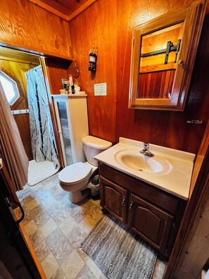 A compact bathroom with wooden walls, a white toilet, a sink, and a mirror.