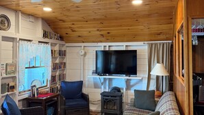 A cozy living room with a fireplace, a television, and a ceiling fan. - Charming, lake-front, 2-bedroom cabin with AC, WiFi in superb Derby (Derby)