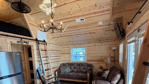 Acogedor interior de cabaña con paredes de madera, un sofá, una mecedora, una mesa de comedor y un refrigerador.