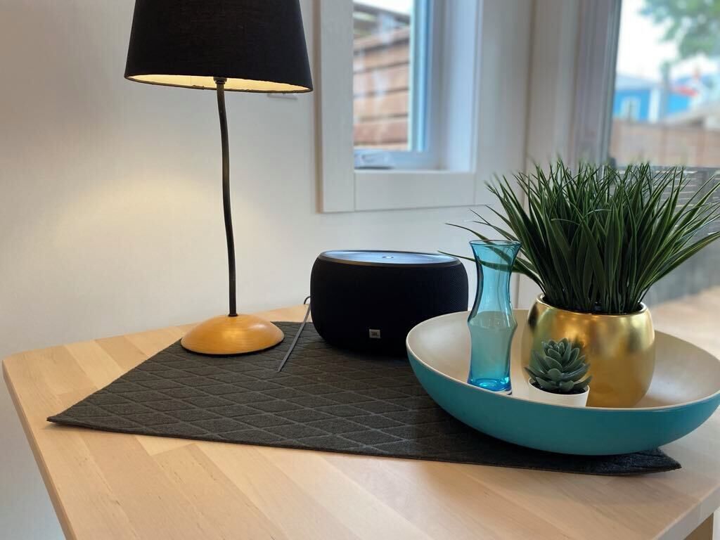 Et moderne værelse med et træbord, en sort lampe, en smart højttaler og en teal skål med planter.