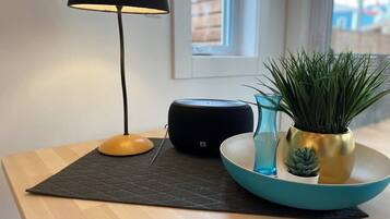 Et moderne værelse med et træbord, en sort lampe, en smart højttaler og en teal skål med planter.