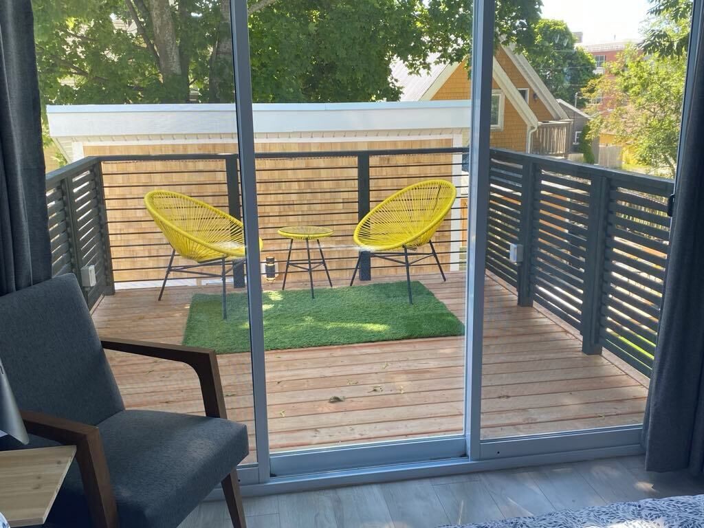 A balcony with a wooden floor, a green rug, and two yellow chairs.