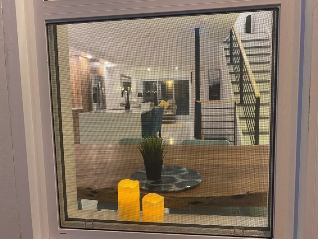 Un intérieur moderne avec un escalier, un coin repas comprenant une table et des bougies, et une vue par une fenêtre.