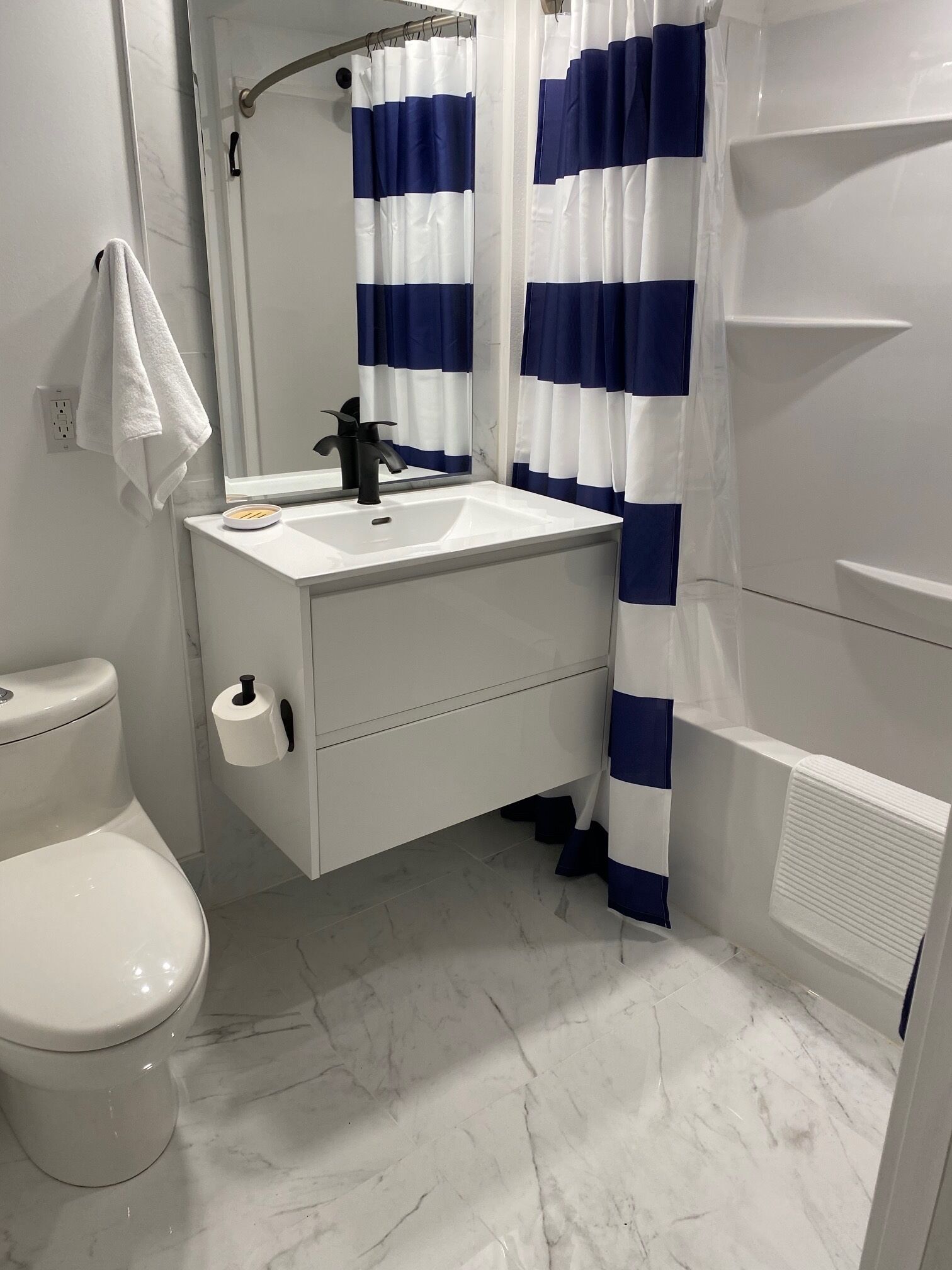 A bathroom with a white toilet, a sink with a black faucet, and a mirror above it. There is a towel hanging on the wall next to the toilet.