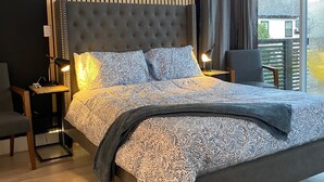 Una camera da letto moderna con testiera trapuntata, coprip letto fantasia e vista all'aperto attraverso ampie finestre.