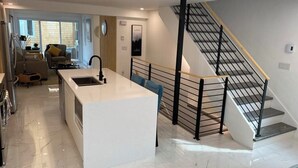 Una cucina moderna con isola centrale, un'area pranzo con divano e tavolo, e una scala con ringhiera in metallo.