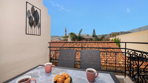 Un balcon avec une table, deux tasses roses, un bol de croissants et une œuvre d’art encadrée.