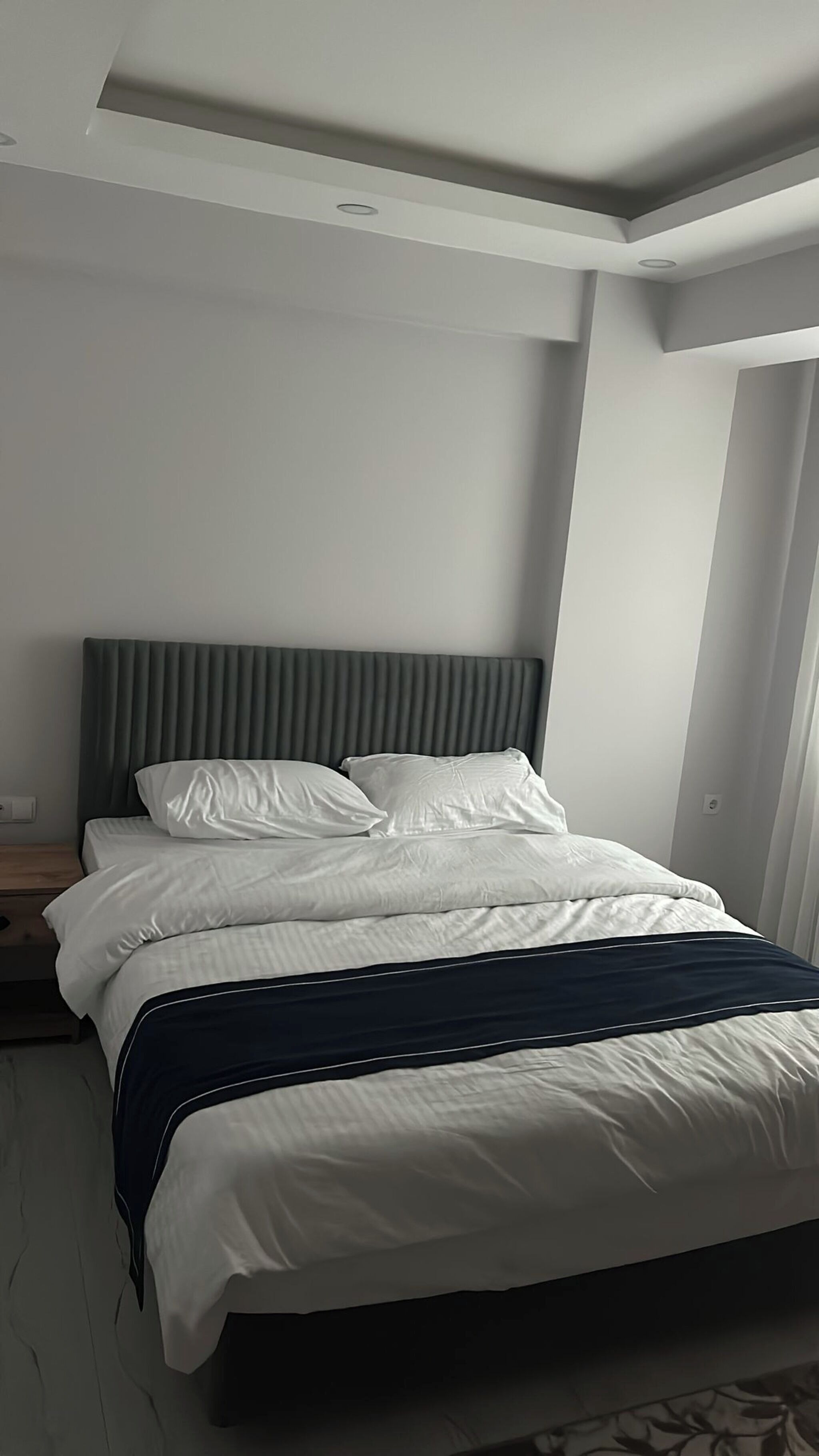A modern hotel bedroom with a large bed, a grey headboard, and a white wall.