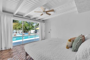 A bedroom with a large bed, a ceiling fan, and a view of a swimming pool through a sliding glass door.