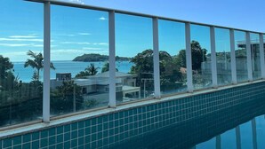 A swimming pool with a clear view of the sea and distant buildings. - Apto Frente Mar Próximo ao Beto Carrero (Penha)