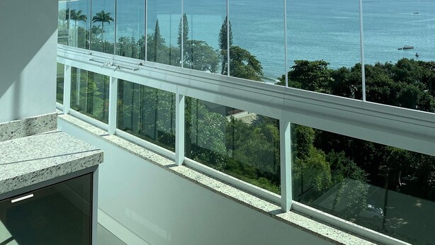 A room with large windows offering a view of a coastal city and the sea. - Apto Frente Mar Próximo ao Beto Carrero (Penha)