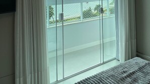 A bedroom with a large window, a bed, and a TV on the wall. - Apto Frente Mar Próximo ao Beto Carrero (Penha)
