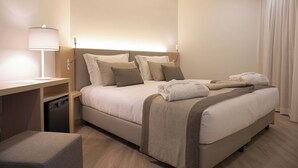 Ein Hotelzimmer mit Bett, Nachttisch, Lampe und einem kleinen Hocker.