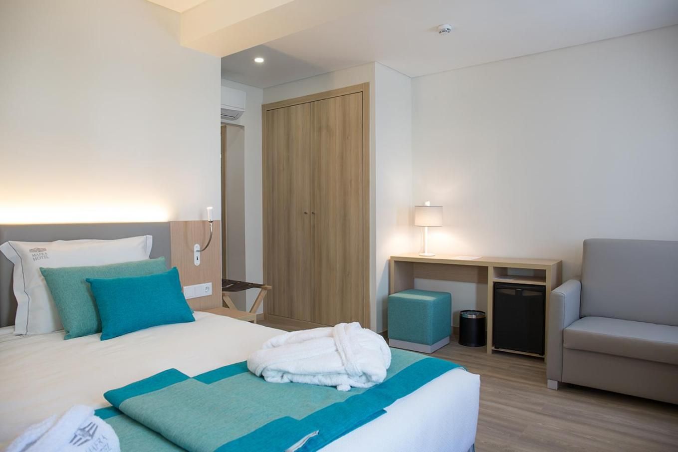 A hotel room with a bed, a desk, a chair, and a wardrobe.
