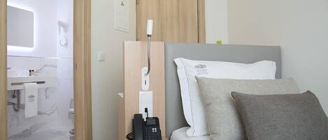 Habitación de hotel con cama, teléfono, mesita de noche, espejo, toalla y puerta.
