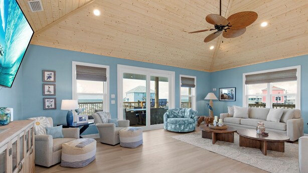 A spacious living room with a wooden ceiling, large windows, and a view of the outside.