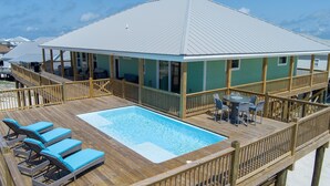 A wooden deck with a pool and lounge chairs, a covered patio, and a view of the ocean.