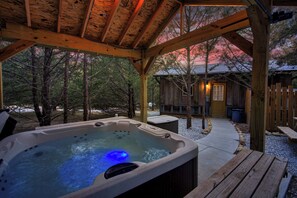 Une terrasse en bois avec un jacuzzi, entourée d’arbres et d’un chalet.