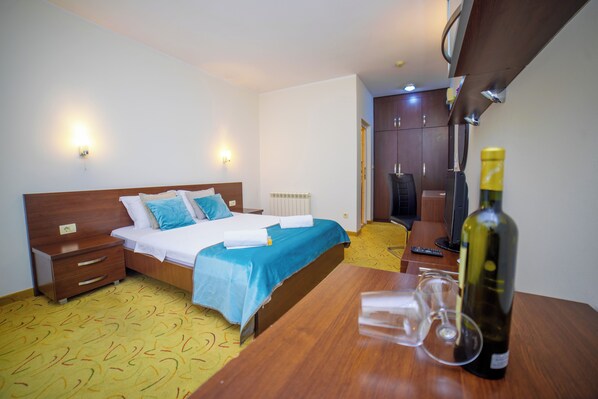 A hotel room with a bed, bedside tables, a wooden desk, a bottle of wine, and a wine glass.