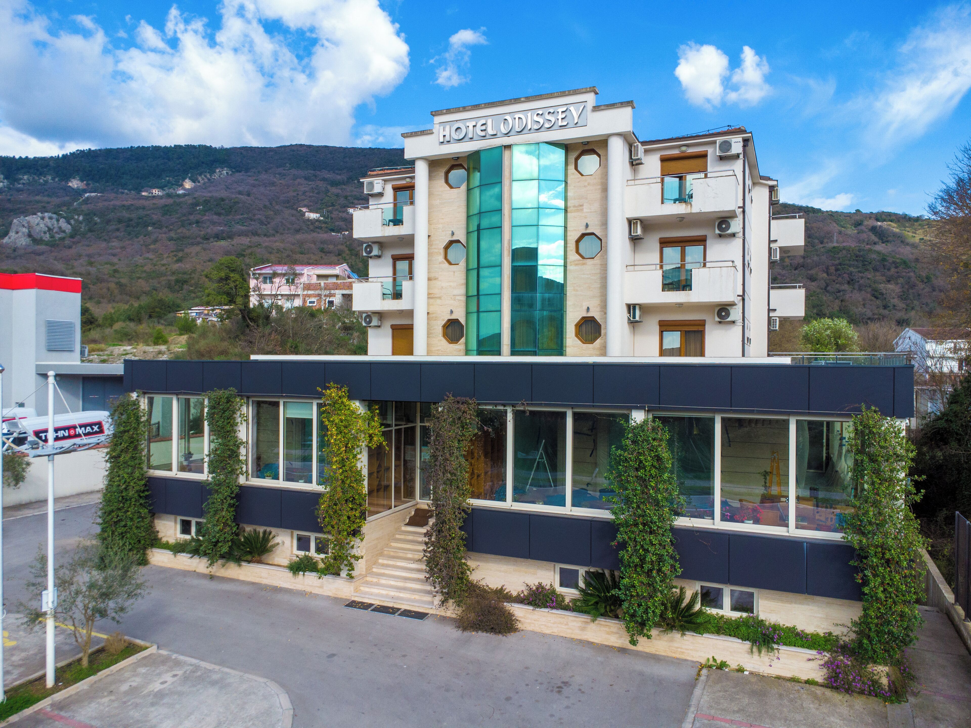 Ein Hotel namens "HOTEL ODISSEY" mit moderner Architektur, großen Fenstern und einem markanten Eingang mit Stufen.