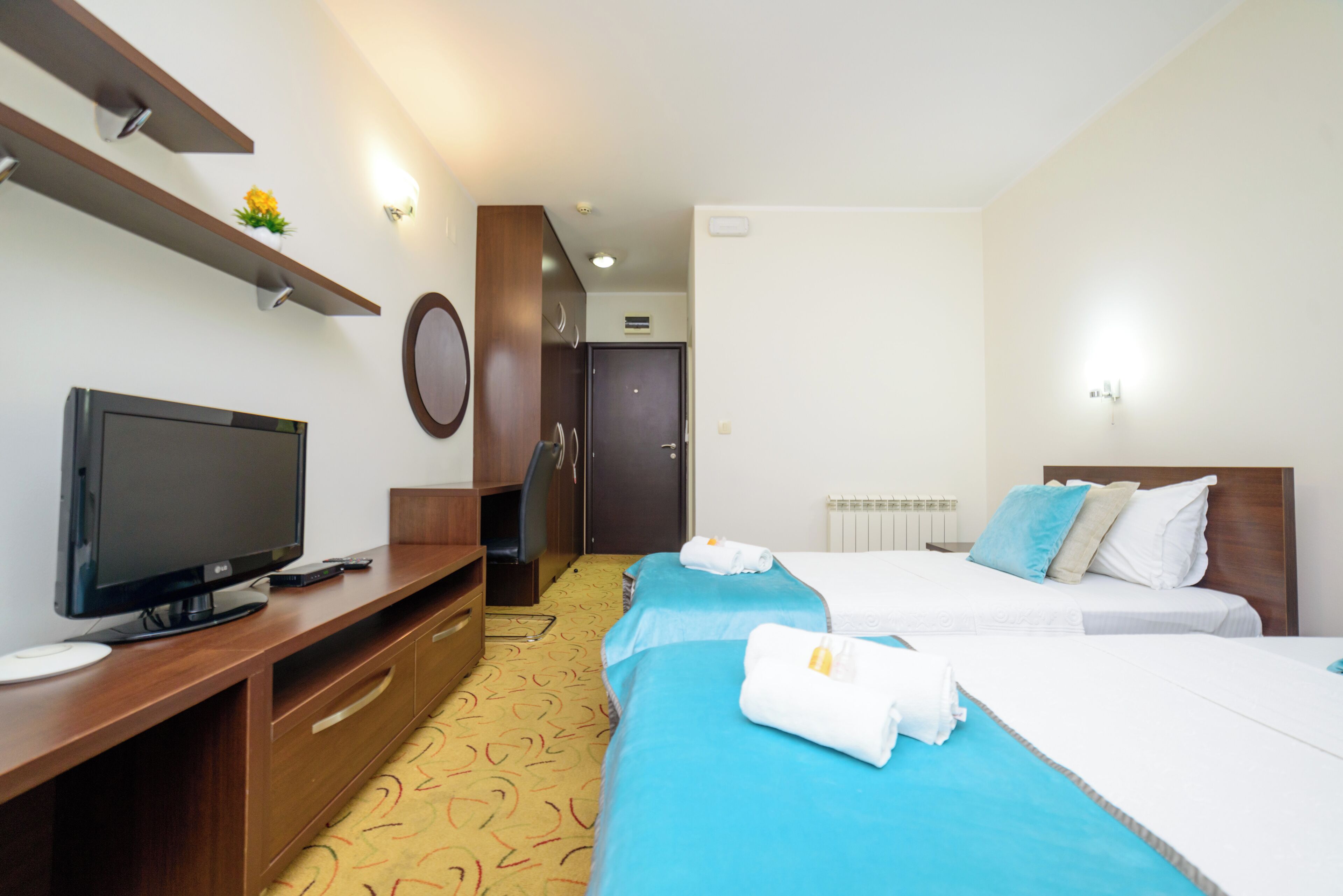 A hotel room with a TV, two beds, a desk, and a wardrobe.