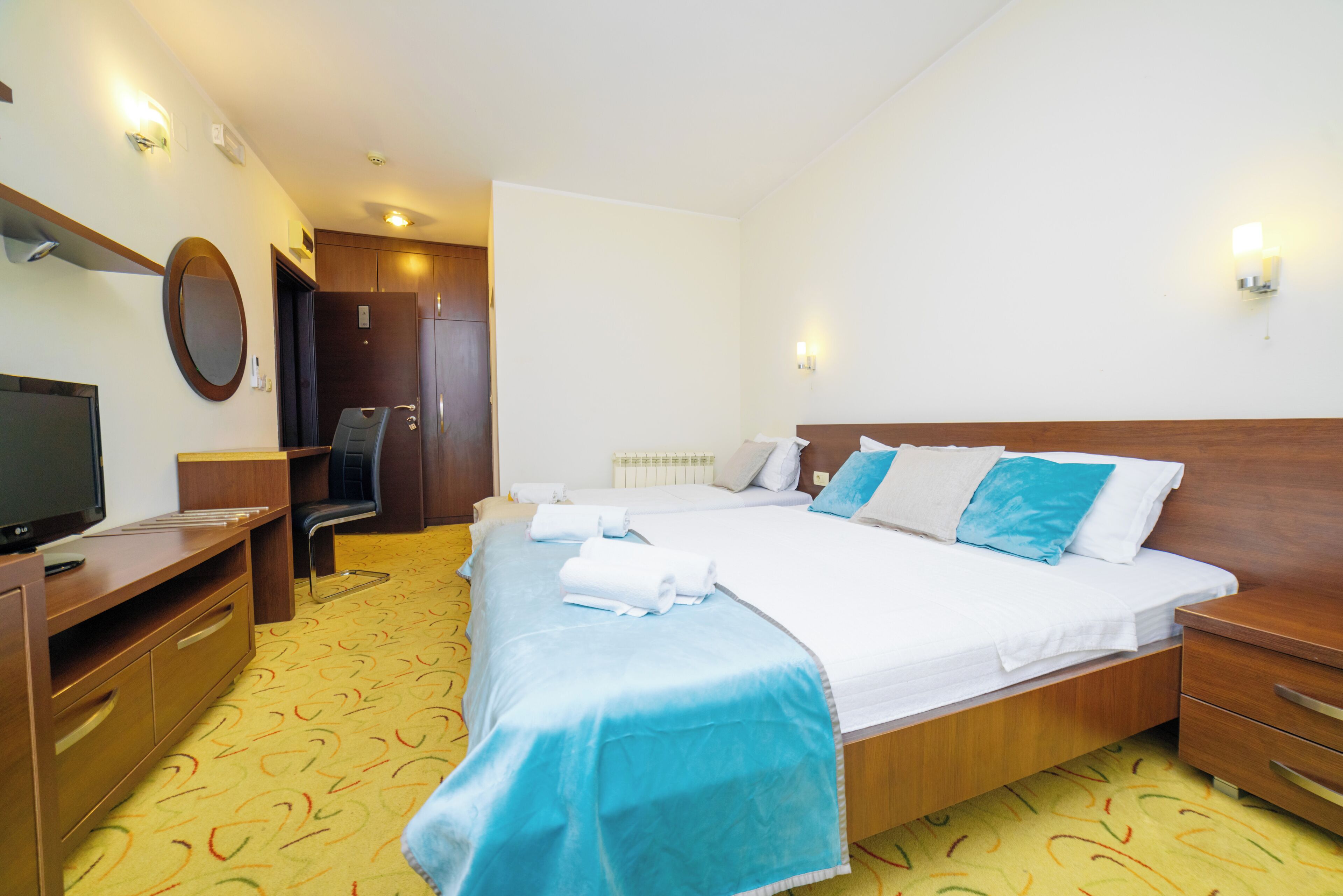 Une chambre d’hôtel avec un lit, un bureau, une chaise, une télévision et une porte de salle de bain.