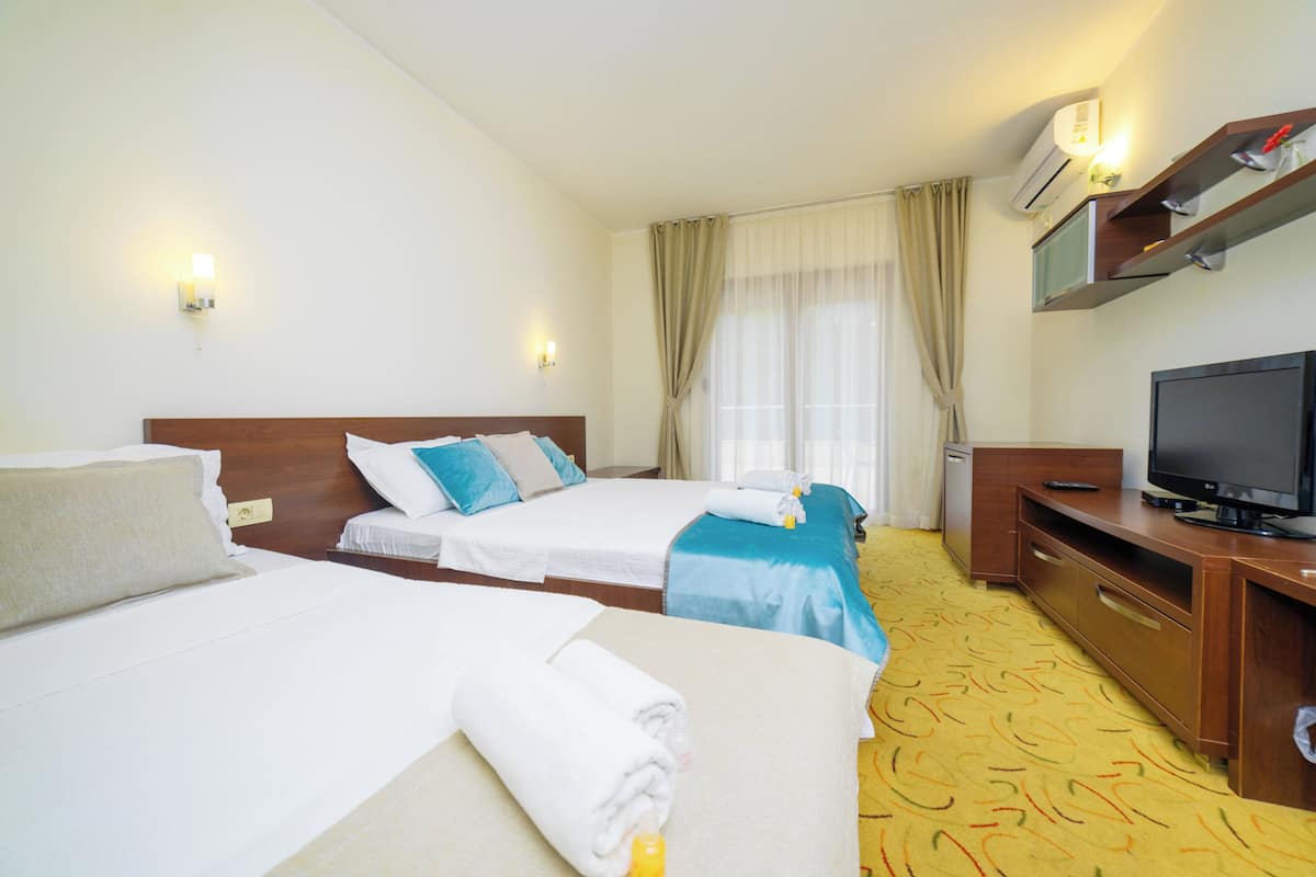 Habitación de hotel con dos camas, televisión, escritorio y ventana con cortinas.