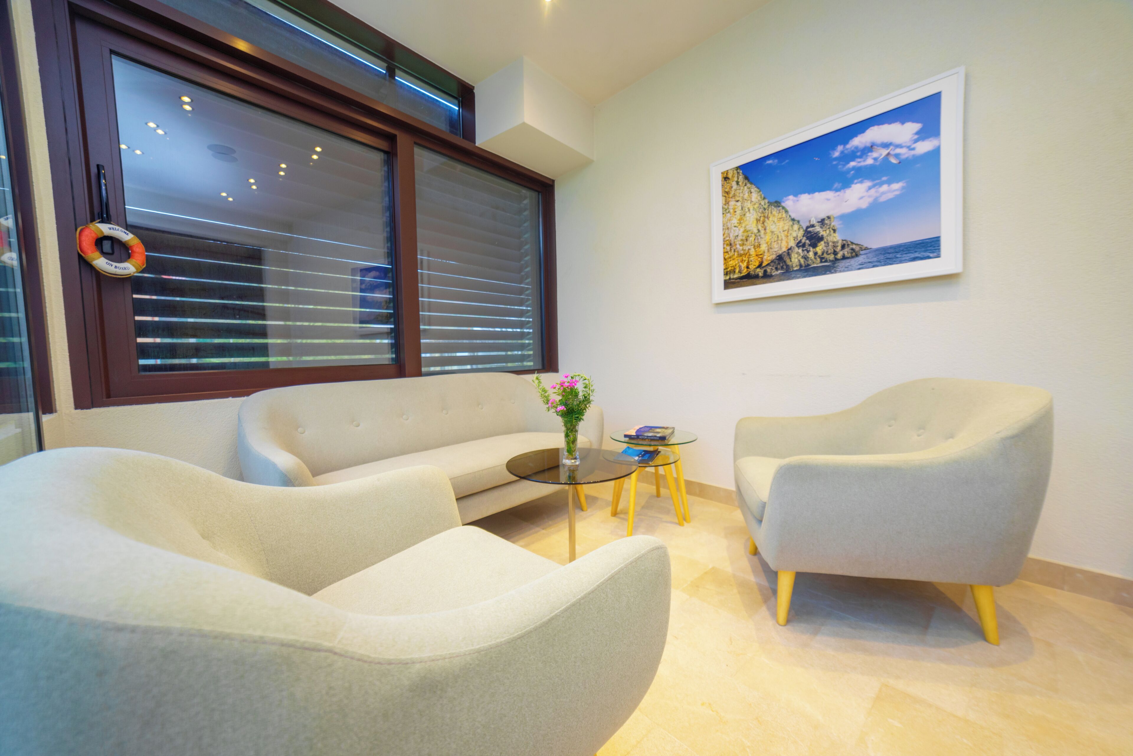 A modern living room with a sofa, armchairs, a glass coffee table, and a framed coastal landscape painting.