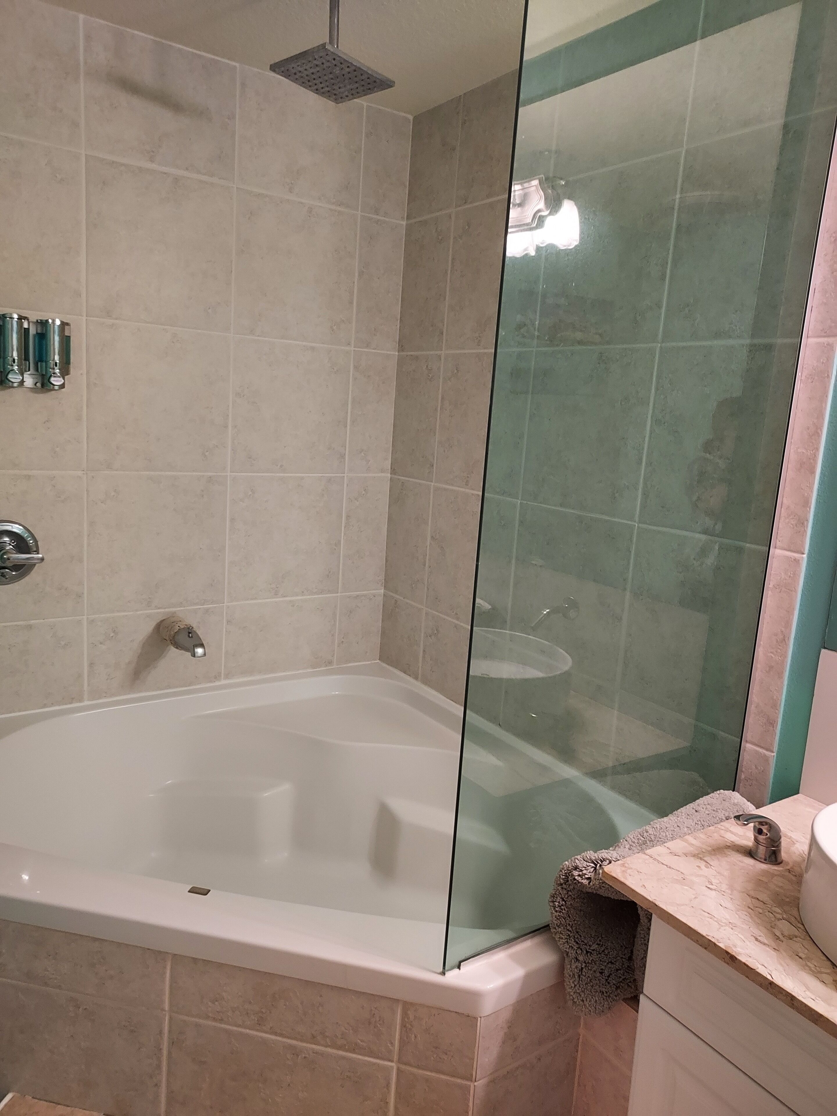 Un baño con bañera de hidromasaje con mampara de vidrio, ducha y lavamanos con toalla.