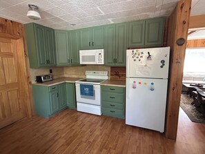 Una cocina con gabinetes verdes, un microondas blanco, un refrigerador blanco y una estufa con una toalla azul.