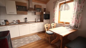 Une cuisine avec des meubles de rangement en bois, un four encastré, une table à manger avec des chaises et une fenêtre ornée de rideaux à motifs floraux.