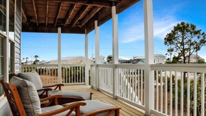Una terraza de madera con dos sillas acolchadas, una barandilla blanca y vistas a edificios y árboles al fondo.
