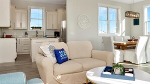 Una sala de estar moderna con un sofá beige, una mesa de centro y un comedor con una mesa de madera y sillas blancas.