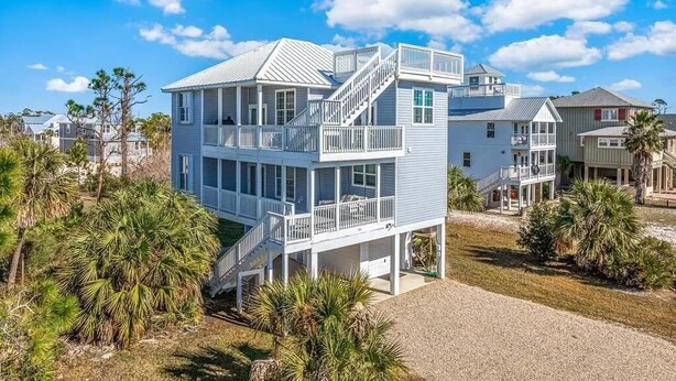Una casa de varios pisos frente a la playa, con un balcón y una escalera que conduce al piso superior.