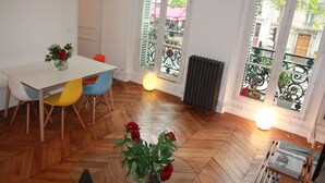 Un comedor con una mesa blanca, sillas coloridas y un suelo de madera en patrón de espiga.