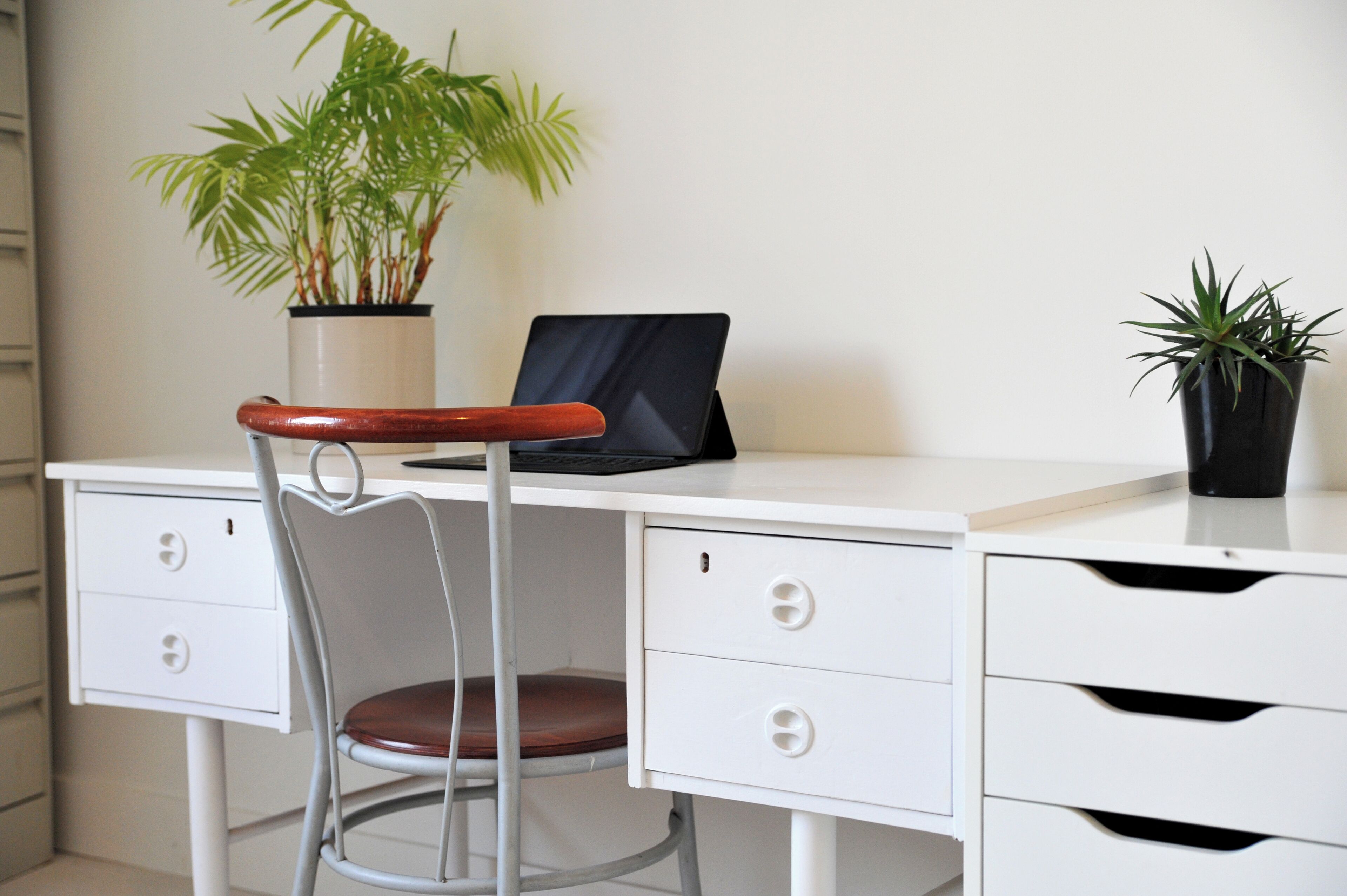 A white desk with a laptop, a chair, and two potted plants.