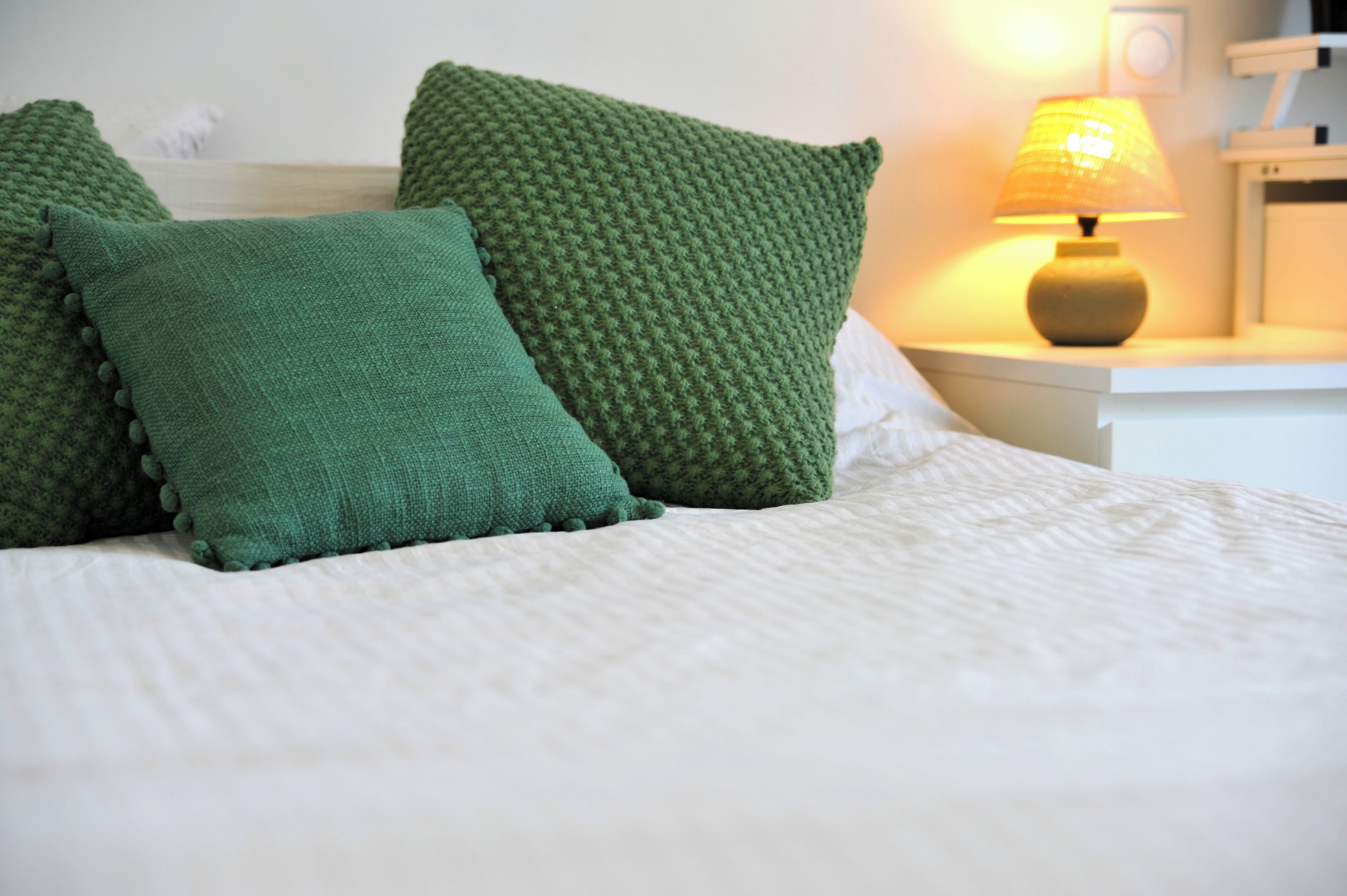 A neatly made bed with green pillows and a bedside lamp.