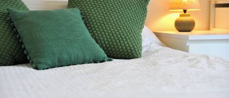A neatly made bed with green pillows and a bedside lamp.