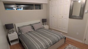 Une chambre à coucher comprenant un lit, deux tables de chevet, une commode, une armoire, un miroir et une fenêtre.