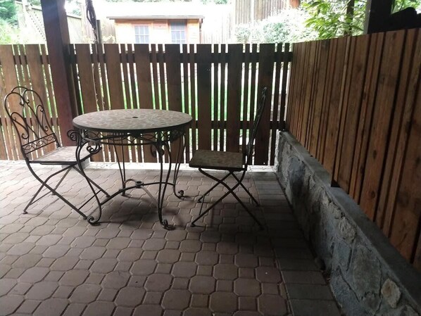 A patio area with a round metal table and two chairs, a wooden fence, and a stone wall.