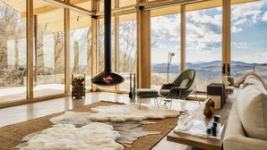 Ein geräumiges Wohnzimmer mit großen Fenstern, einem Kamin, einer Couch und einem Teppich.