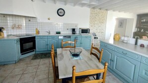 Une cuisine avec des meubles de rangement bleus, une table à manger avec des chaises, un four à micro-ondes et un évier.