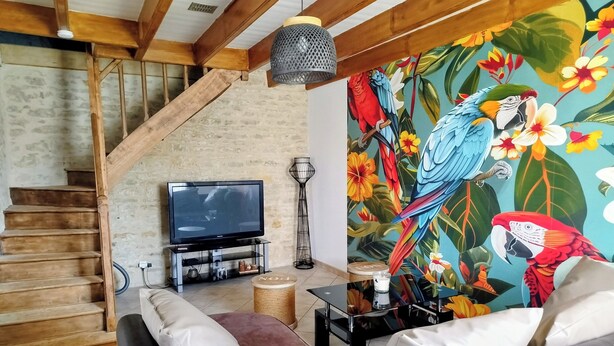 Un salon comprenant un canapé, un téléviseur, un escalier et une fresque murale aux couleurs vives représentant un paysage tropical.